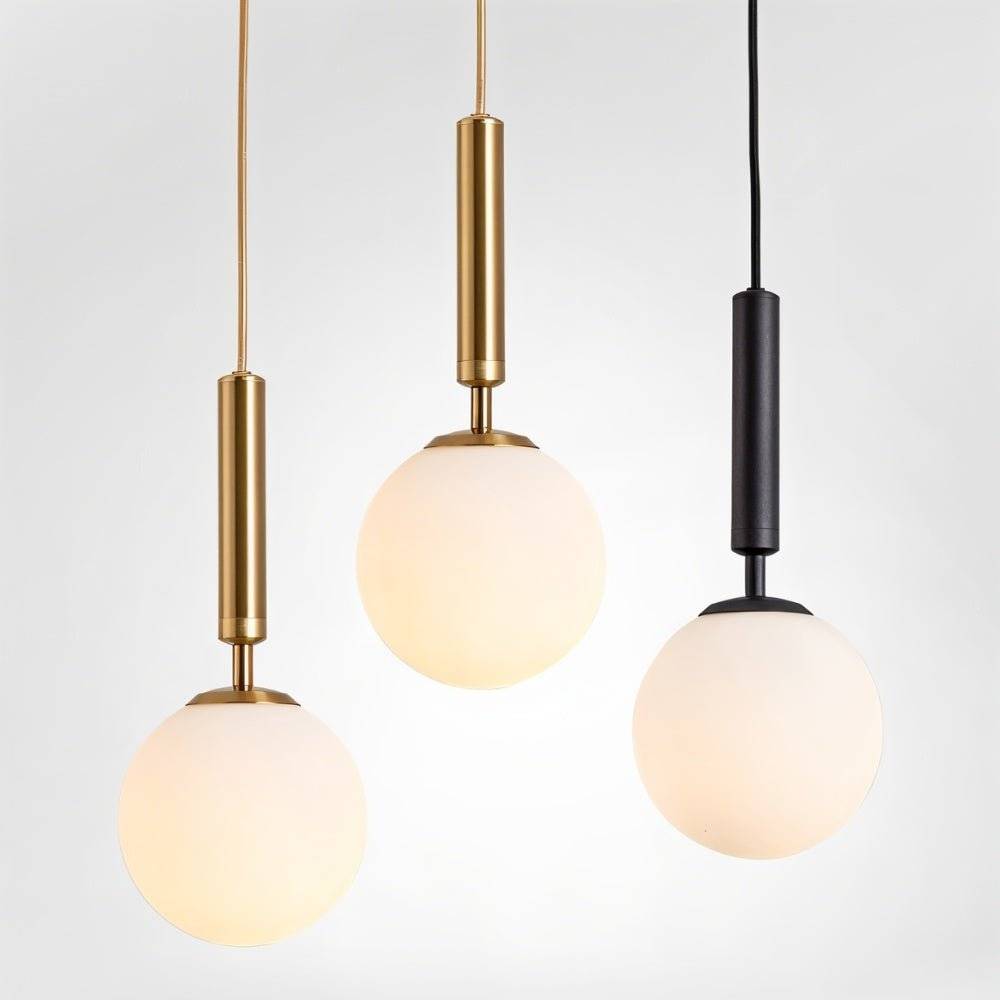 Clérachic globe pendant lights in brass and black finishes grouped together, each with a glowing white glass shade.