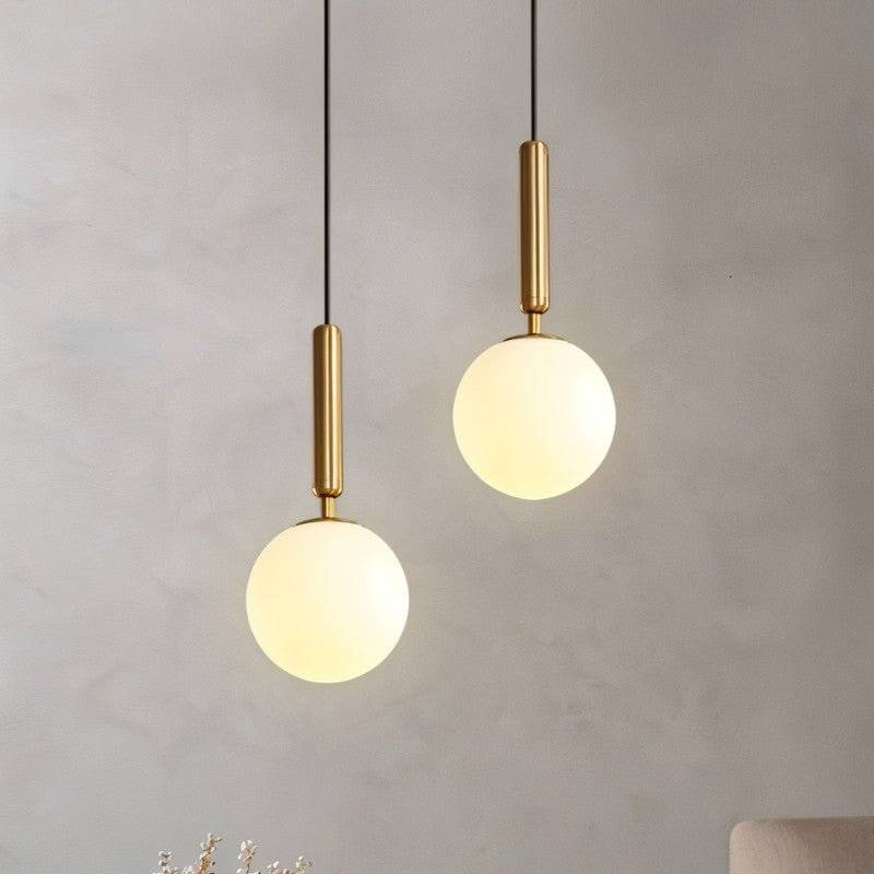 Clérachic brass pendant lights with white globe shades hanging at staggered heights against a plaster wall.