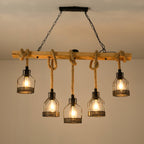 This Clérachic pendant light switched on beneath a beige ceiling, its five filament bulbs glowing inside black mesh cages.