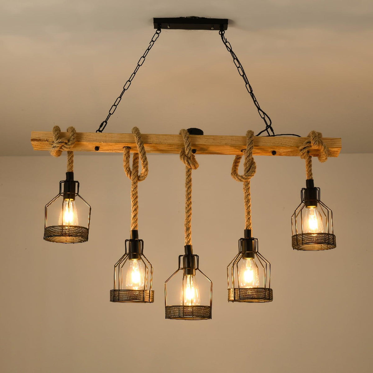 This Clérachic pendant light switched on beneath a beige ceiling, its five filament bulbs glowing inside black mesh cages.