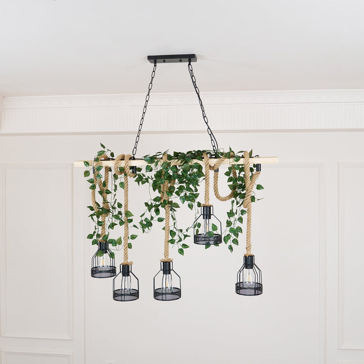 A Clérachic pendant light dressed with trailing green ivy along the beam, shown against a white panelled wall.