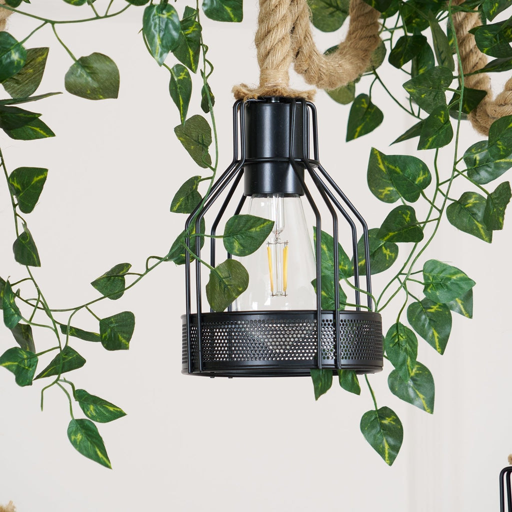Close view of a single black cage with a clear bulb on this Clérachic pendant light, with green leaves around it.
