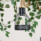 Close view of a single black cage with a clear bulb on this Clérachic pendant light, with green leaves around it.