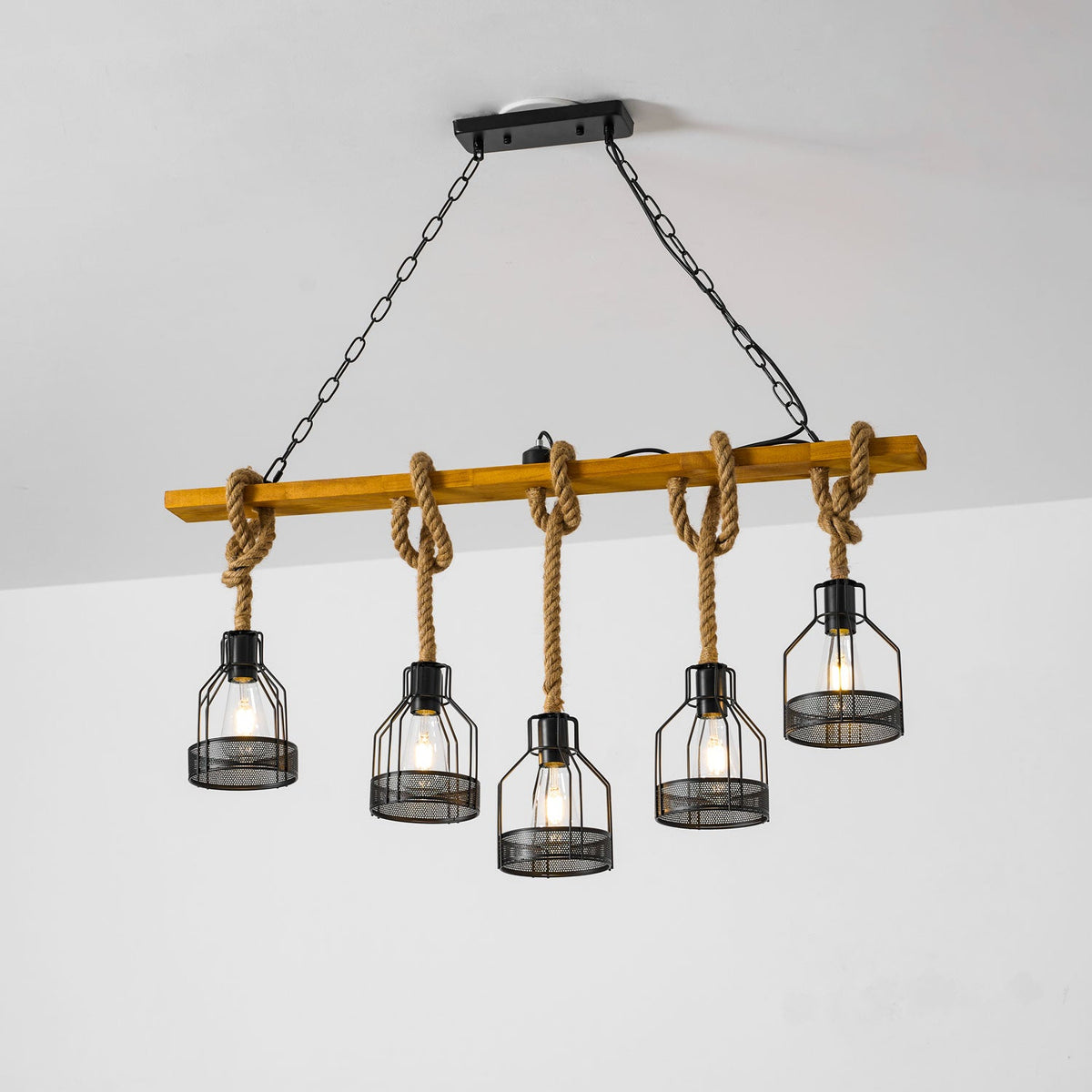 Clérachic pendant light with five caged bulbs, hanging at staggered heights on knotted rope from a warm wooden beam.