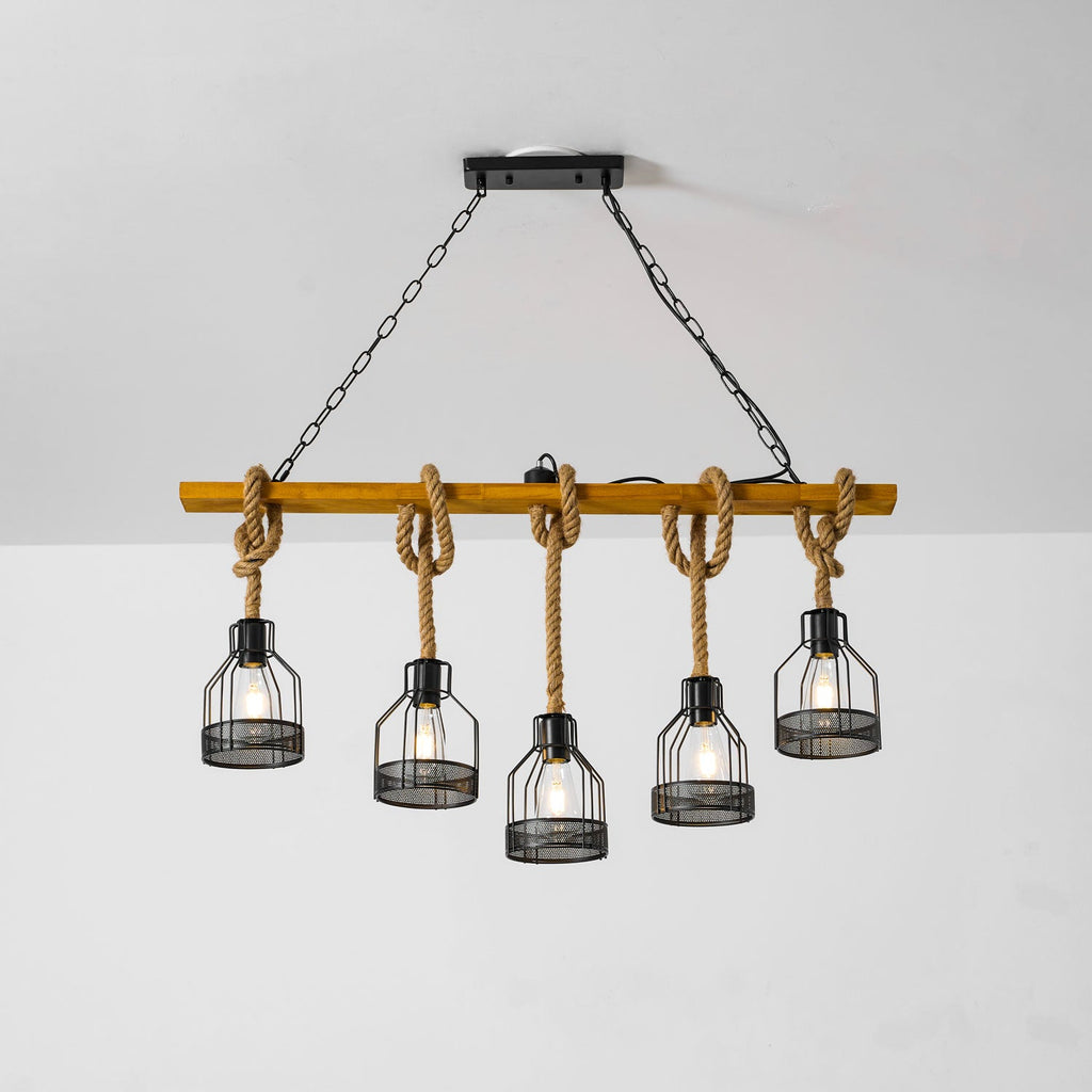 A wooden-beam Clérachic pendant light on two black chains, with five bulbs lit in iron mesh cages against a white wall.