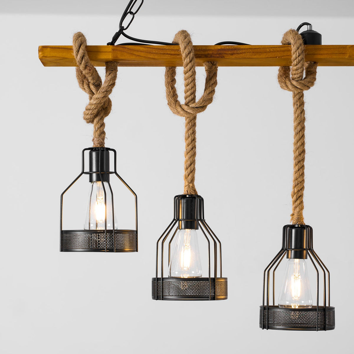 Close view of three black mesh cages with clear filament bulbs hanging on knotted hemp rope from a Clérachic pendant light.