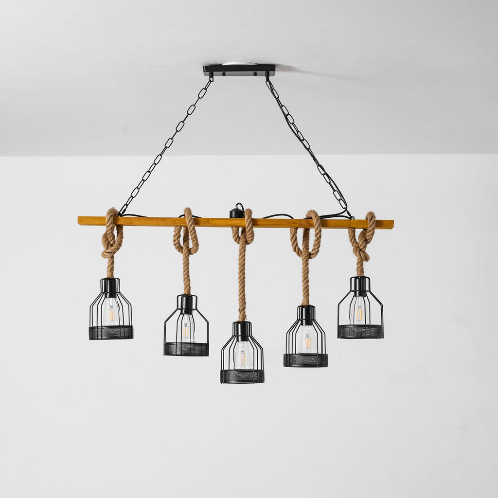 A Clérachic pendant light on its black canopy and chains, with five caged bulbs on rope hanging against a pale grey wall.