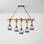 A Clérachic pendant light on its black canopy and chains, with five caged bulbs on rope hanging against a pale grey wall.