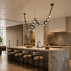 Black Clérachic linear pendant draped in two loops above a stone-clad kitchen island with leather-topped bar stools.