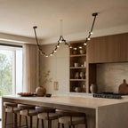This Clérachic black pendant light swoops across a kitchen above a pale island, with open shelving and a wide window beside it.