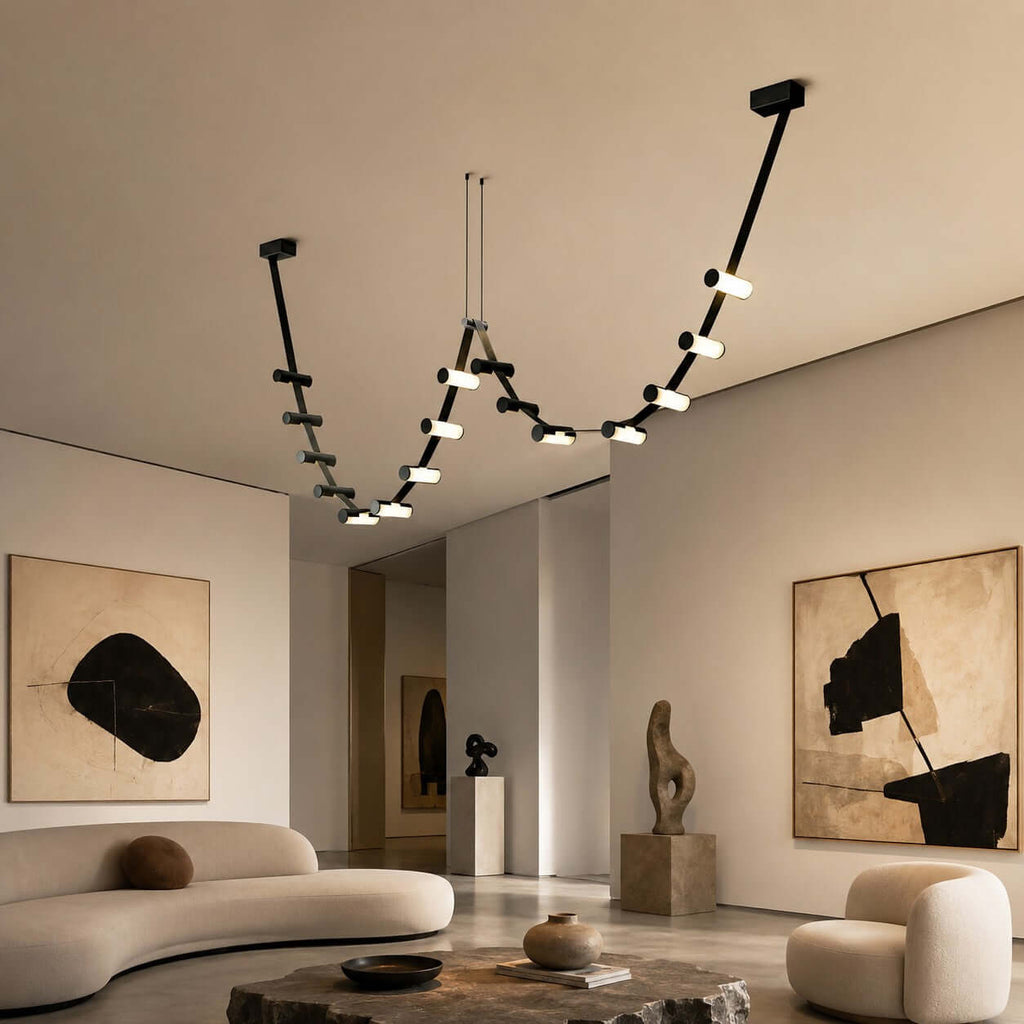 Long Clérachic linear pendant with lit cylinders hangs in a high-ceilinged living room with a curved cream sofa and large abstract art.