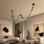 Long Clérachic linear pendant with lit cylinders hangs in a high-ceilinged living room with a curved cream sofa and large abstract art.