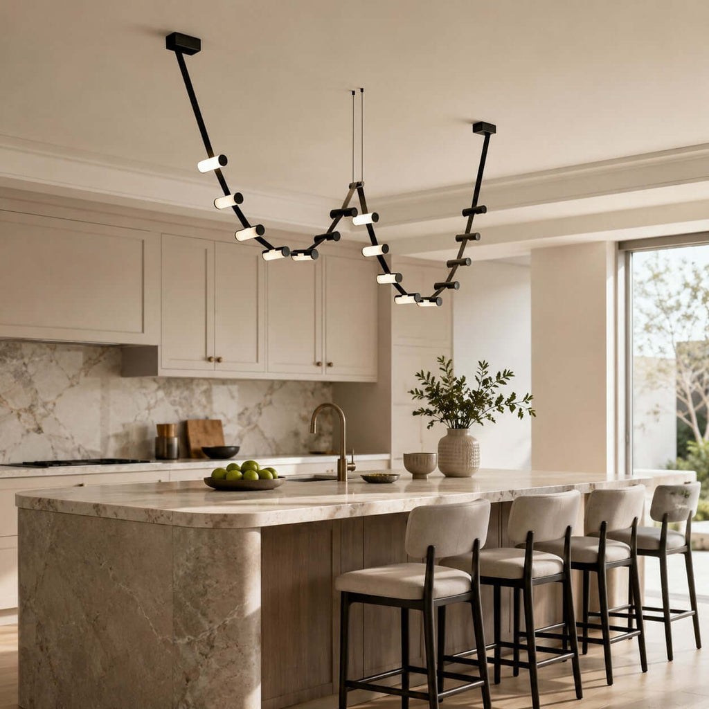 Black Clérachic pendant light looping across a bright kitchen with cream cabinets, a marble splashback and a stone island.