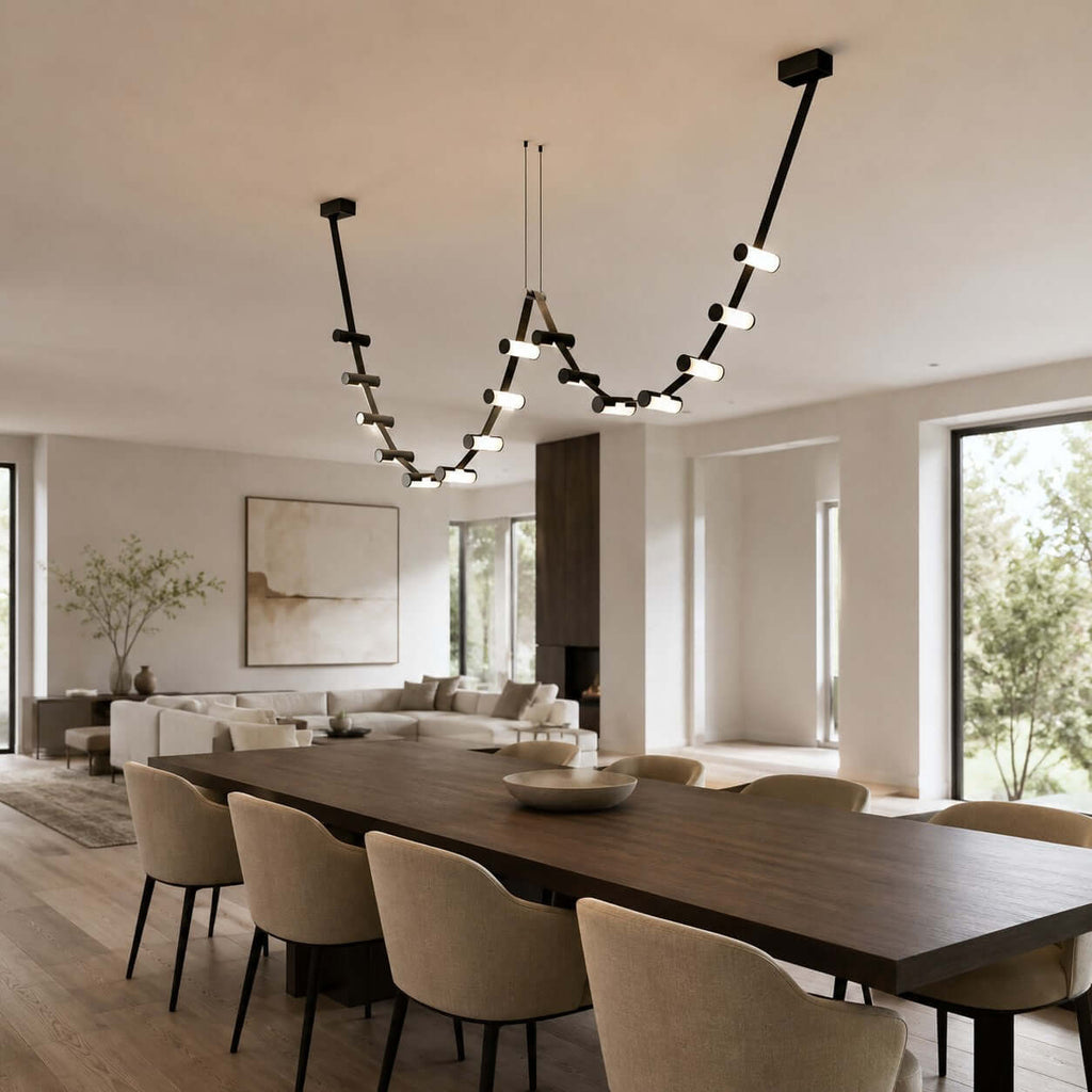 Over a long dark dining table in an open-plan room, a Clérachic linear pendant dips in two loops of lit cylinders.