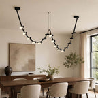 This Clérachic black linear pendant hangs above a walnut dining table, with a sideboard and an olive tree behind.