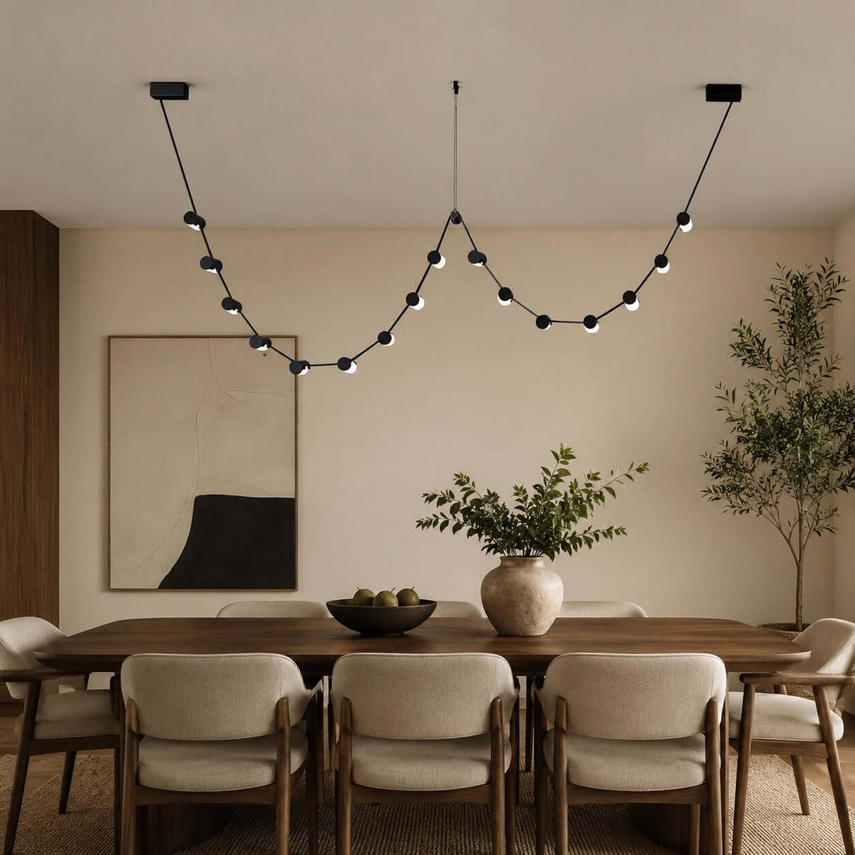 This Clérachic pendant light, a string of small black beads in two loops, hangs above a dining table with upholstered chairs.