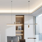 Long bar pendant from Clérachic in an office with warm shelving, a cove-lit ceiling, a desktop screen and a window with blinds.