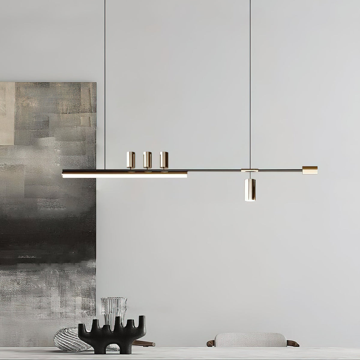 Long bar of this Clérachic pendant lit in front of a grey wall and a textured abstract canvas, with a dark sculptural piece below.