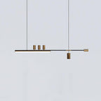 This Clérachic pendant on a cool pale-grey backdrop, showing the lit bar, three brass-toned cylinders and a hanging spot.