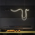 Clérachic long black bar pendant with three spot heads and a looping white LED tube, above a dining table in a dark room.