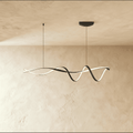 Clérachic twisting black ribbon LED pendant lit warm white, hung from two slim cords below a ceiling plate against a limewash wall.