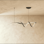Clérachic twisting black ribbon LED pendant lit warm white, hung from two slim cords below a ceiling plate against a limewash wall.