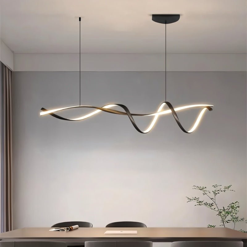 Clérachic black ribbon pendant glowing above a dining table with grey chairs, in front of a soft grey wall and a leafy branch.