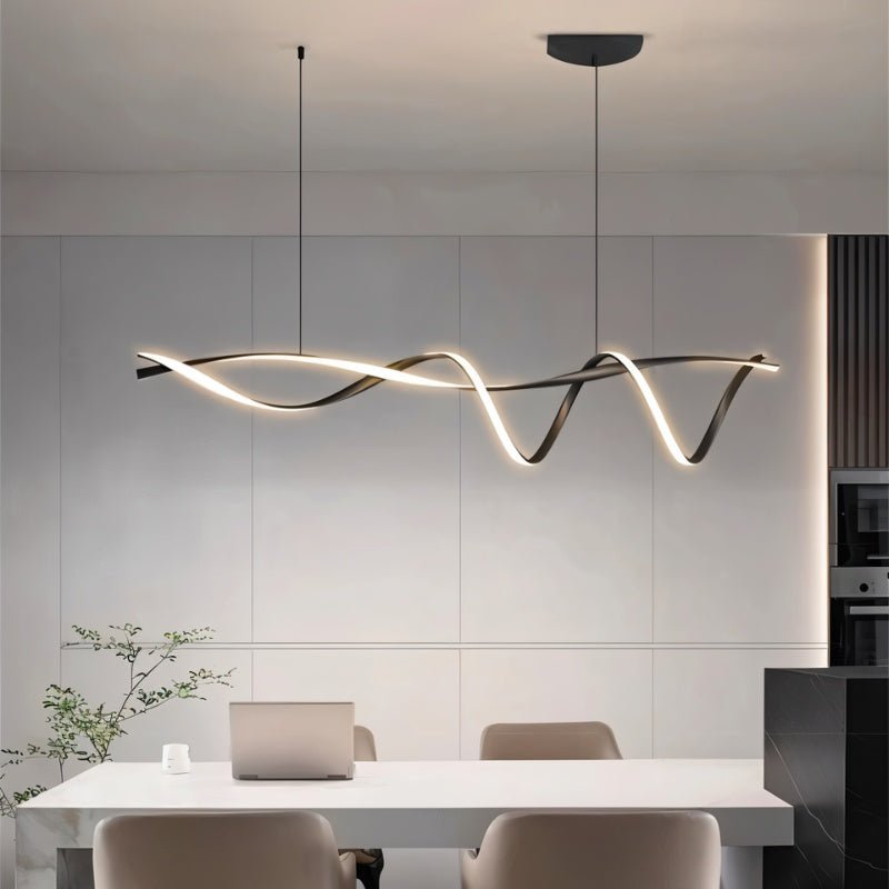 Clérachic twisting black LED pendant hung over a white dining table in a kitchen with panelled grey walls and a black marble island.