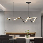 Clérachic glowing ribbon pendant above a kitchen island and dining table, with a glass vase, dark chairs and a marble-veined worktop.