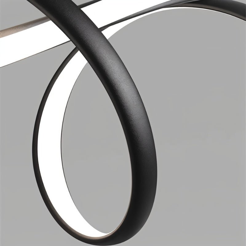 Macro of the Clérachic pendant's textured matt black ribbon curling in a loop, with the white LED diffuser glowing along its inner edge.