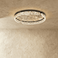 Clérachic round ceiling light with a black metal frame and a lit marbled glass ring, seen against a textured plaster ceiling.