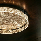 Close-up of the Clérachic ceiling light, its cracked-ice marbled glass ring and centre glowing warmly against a dark wood ceiling.