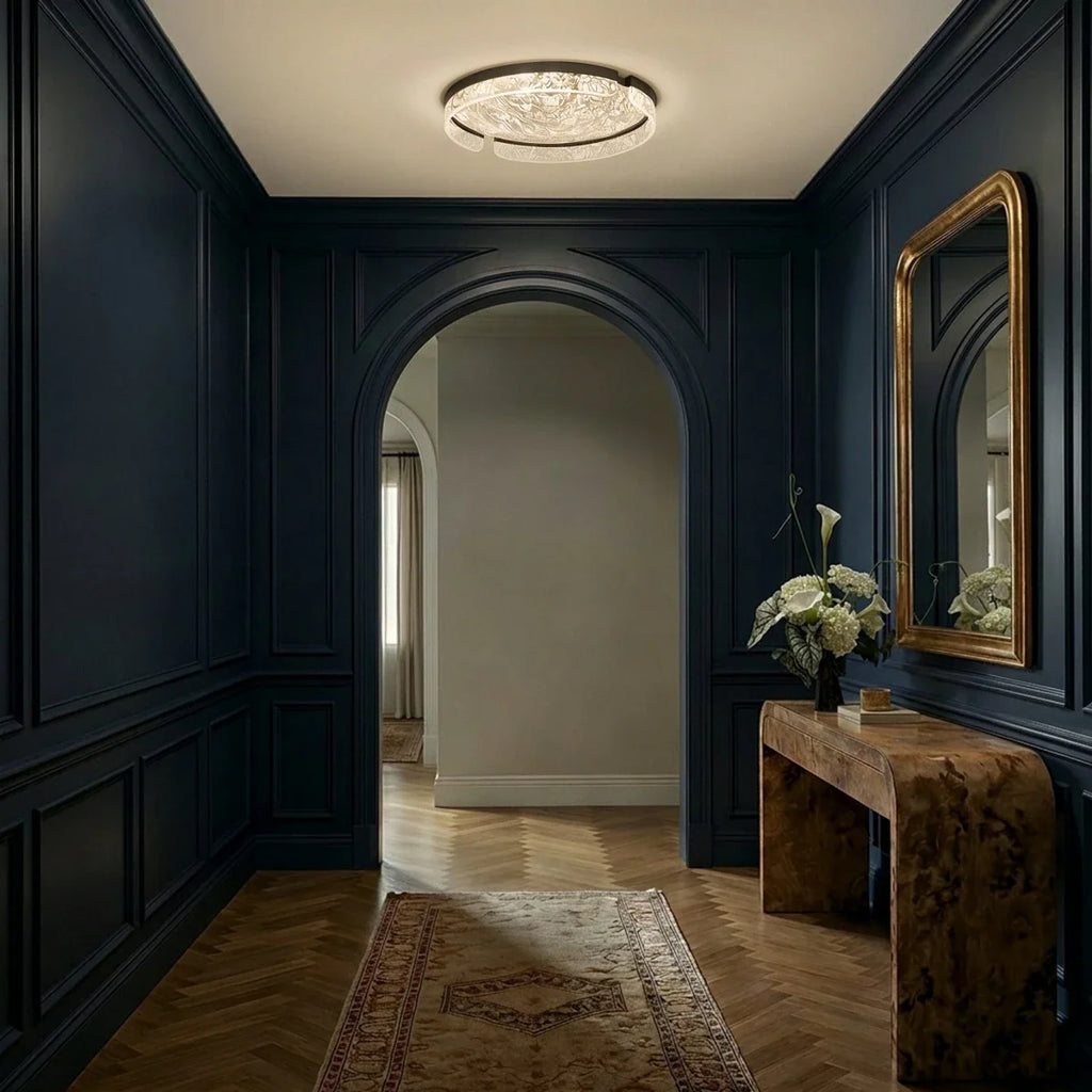 Clérachic round ceiling light lit in a navy panelled hallway with an arched doorway, herringbone floor and a gilt mirror.