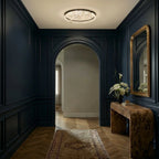 Clérachic round ceiling light lit in a navy panelled hallway with an arched doorway, herringbone floor and a gilt mirror.