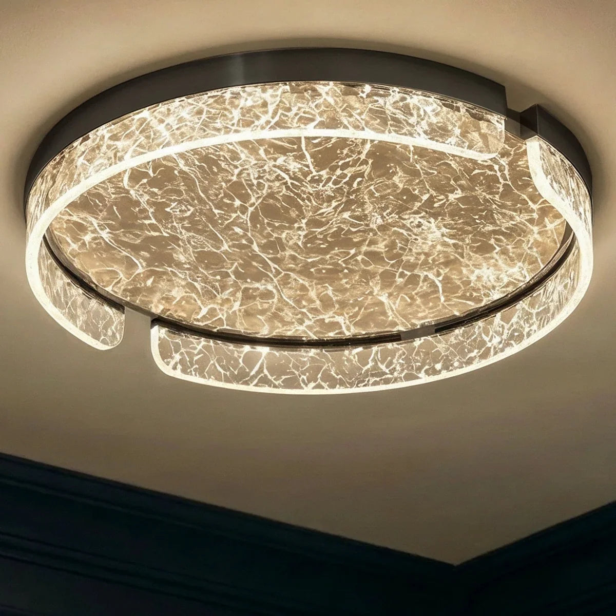 Clérachic round ceiling light viewed from below, lit, with a black metal rim and bright marbled glass ring and centre.