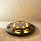 A round black solar disc light glows warm amber from its slatted sides on a plain studio floor in this Clérachic hero shot.