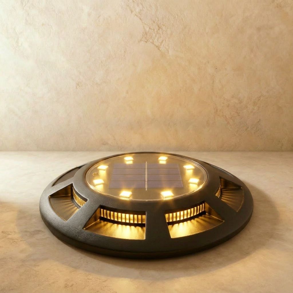 A round black solar disc light glows warm amber from its slatted sides on a plain studio floor in this Clérachic hero shot.