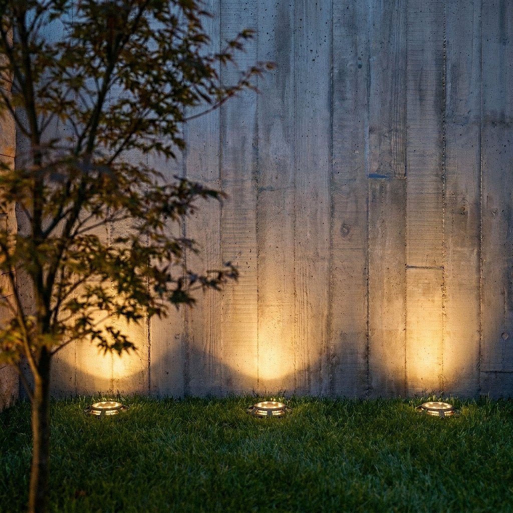 At night, three black solar disc lights sit flush in a lawn, uplighting a board-formed concrete wall in this Clérachic lifestyle shot.