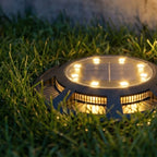 A close-up on one black solar disc light glowing warm amber through its slatted sides, set in green grass, Clérachic detail shot.