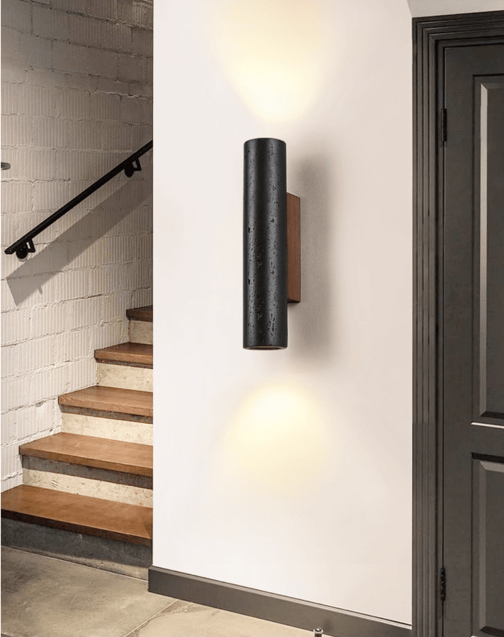 Light spills up and down from a Clérachic black stone wall light beside a dark doorway and a timber staircase.