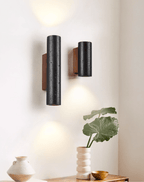 A tall and a short black Clérachic wall light side by side above a console with a pale vase and a large green leaf.