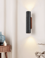 A Clérachic wall light sends light both up and down beside a ribbed wooden console, a blue vase and a trailing plant.