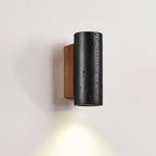 Close view of a short Clérachic black travertine cylinder on its walnut plate, light pooling down the wall below.