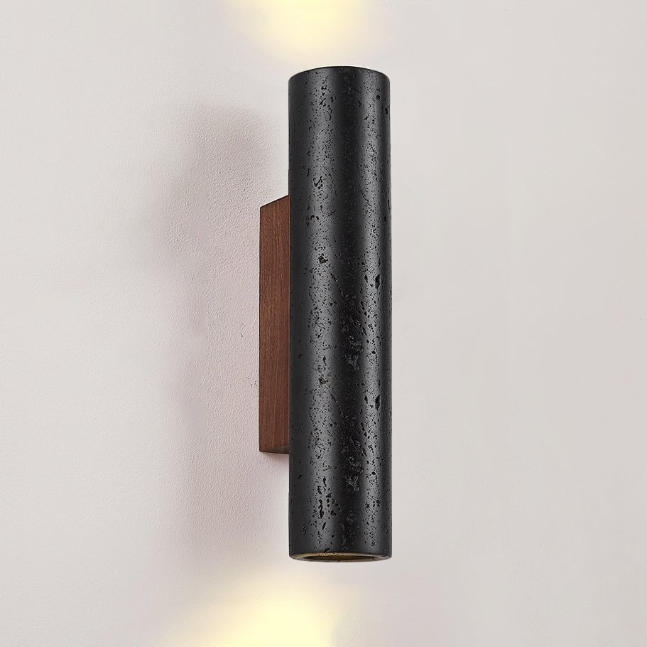 A Clérachic cylinder light with up and down beams, showing its pitted black stone surface and the walnut plate behind.