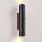 A Clérachic cylinder light with up and down beams, showing its pitted black stone surface and the walnut plate behind.