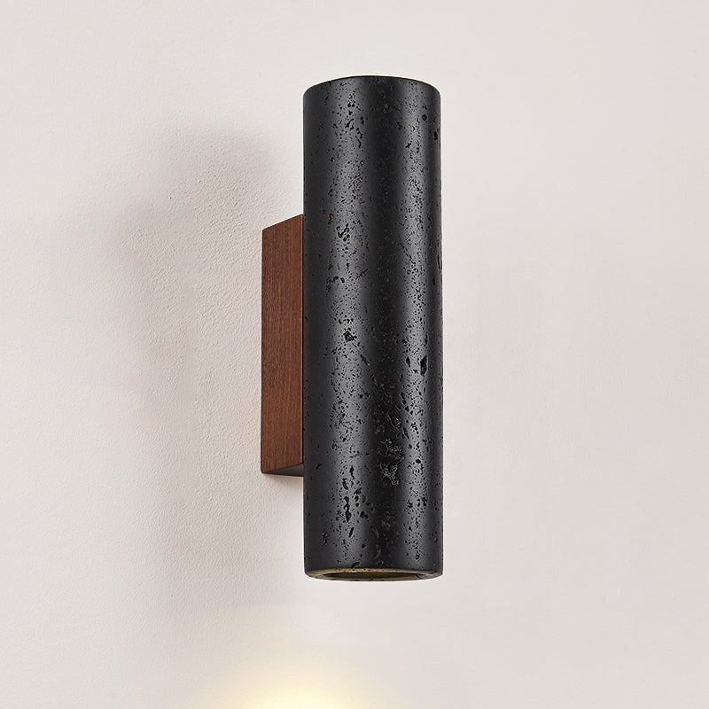 A close, front-on look at the speckled black travertine of a Clérachic wall light and its walnut backplate.