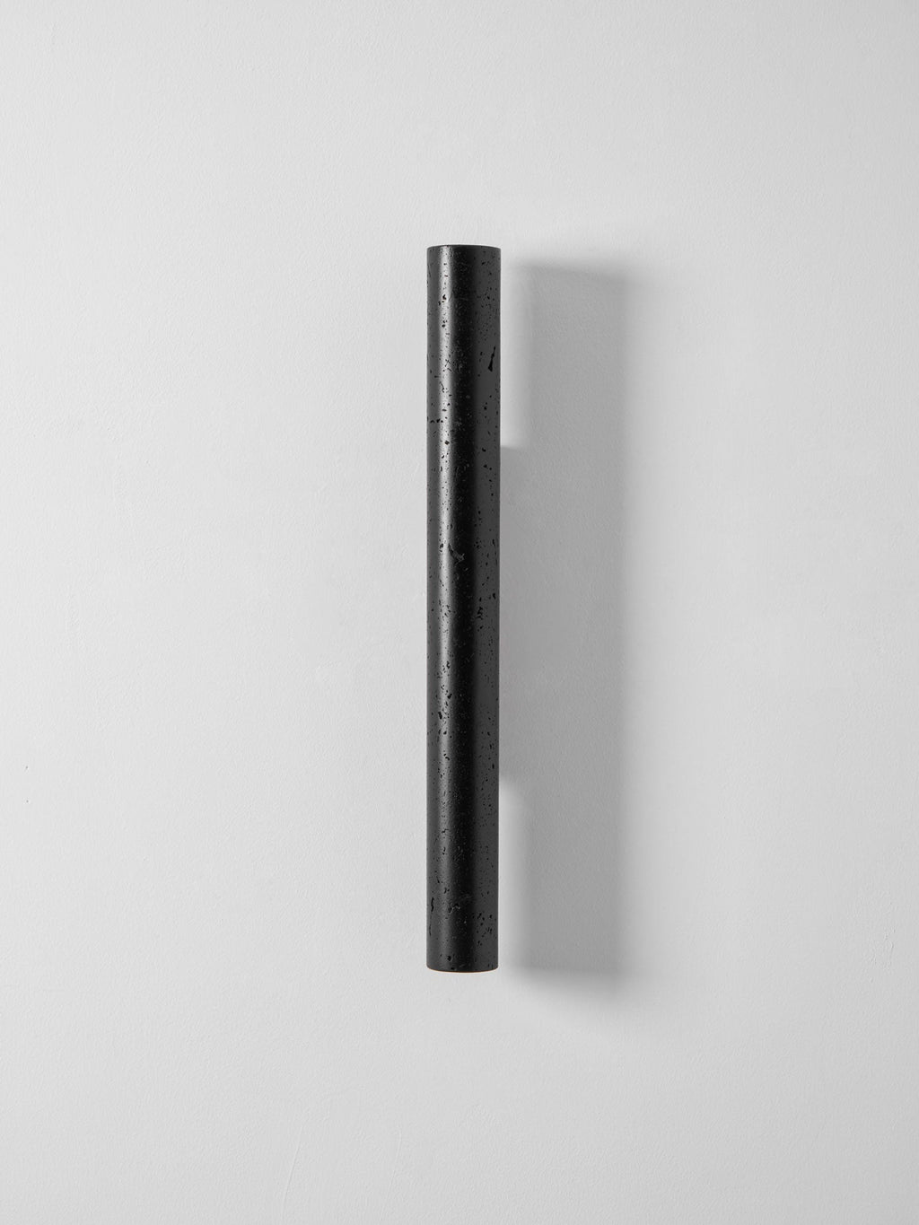 A slim, tall black Clérachic cylinder wall light, unlit, on a pale grey wall.