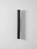 A slim, tall black Clérachic cylinder wall light, unlit, on a pale grey wall.