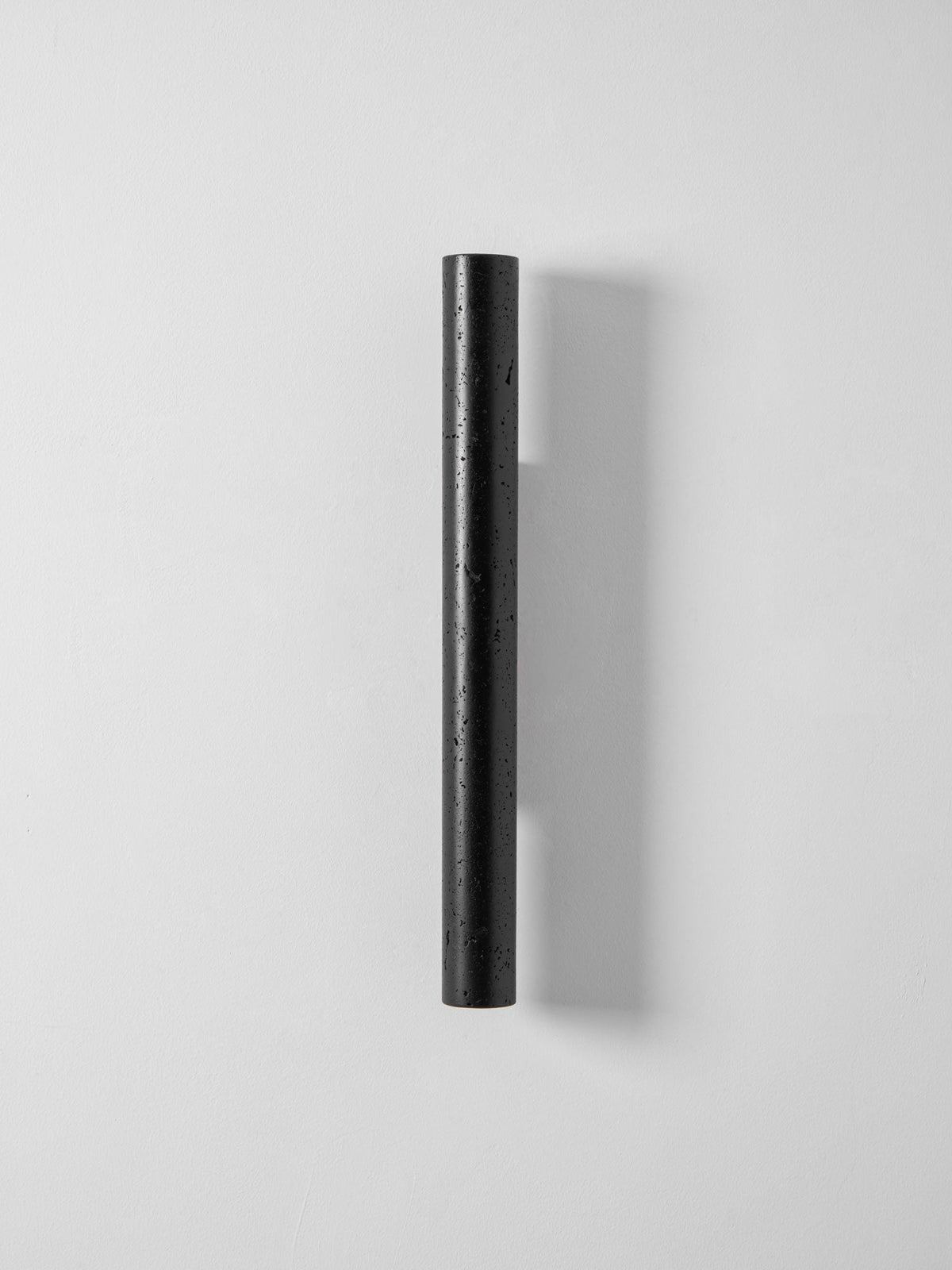 A slim, tall black Clérachic cylinder wall light, unlit, on a pale grey wall.