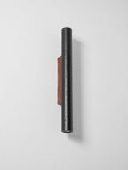 A tall, narrow Clérachic black cylinder on a walnut plate, switched off, seen at an angle against a pale wall.